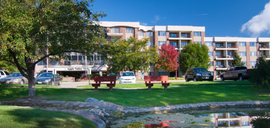 Panoramic photo of Apple Valley Village, with green, leafy trees and a walking path.