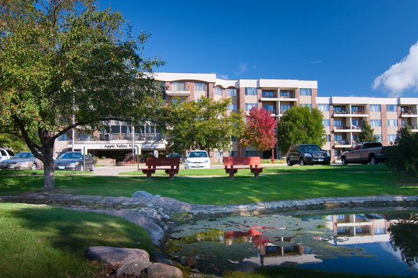 Panoramic photo of Apple Valley Village, with green, leafy trees and a walking path.