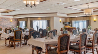 Dining room at Apple Valley Village with tables, chairs, large windows, and natural light.