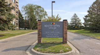 Apple Valley Village entrance sign with landscaping and roadside view.