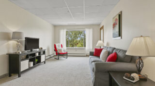 Living room with sofa, chairs, and windows at Apple Valley Village.