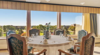 Dining room at Apple Valley Village with tables, chairs, and large windows with outdoor views.